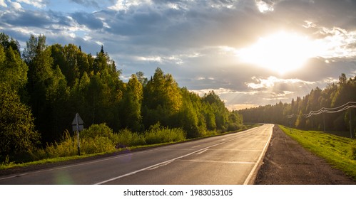 Country road with markings in the middle of the forest. Path and forward movement in the sun. Beautiful, green forest in the spring at sunset. Concept for success in the future goal and passing time