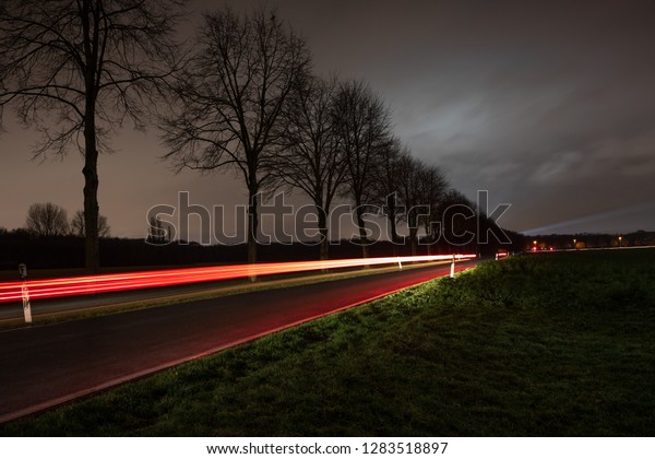 A\
country road with a moving car at night with grey\
sky.