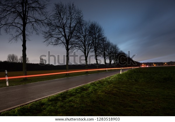 A
country road with a moving car at night with blue
sky.