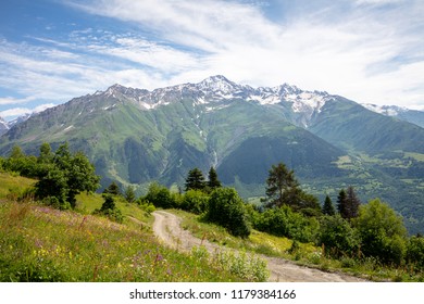 country road on meadow and mountain with snowy peak in sunny day