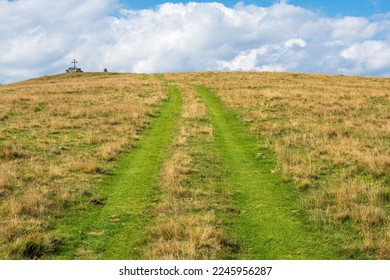 Country road through grassy meadow in mountains, sky with clouds on the horizon, Gurktal Alps, Carinthia, Austria.