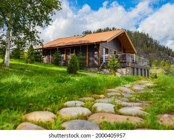 Country vacation in summer. Cottage near pine forest and rock. Cottages for rent concept. Suburban cottage vacation in nature. Stone path next to cottage with terrace. Suburban rental houses.