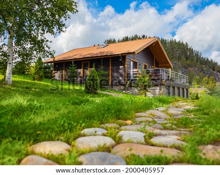 Country vacation in summer. Cottage near pine forest and rock. Cottages for rent concept. Suburban cottage vacation in nature. Stone path next to cottage with terrace. Suburban rental houses.
