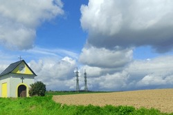 Countryside Landscape, Small Chapel At The Field, In The Background Of High Voltage And Blue Sky With Clouds