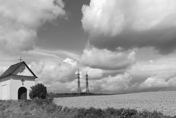 Countryside Landscape, Small Chapel At The Field, In The Background Of High Voltage And Sky With Clouds, Black And White Photo