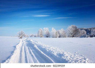 Countryside road through winter field with forest on a horizon