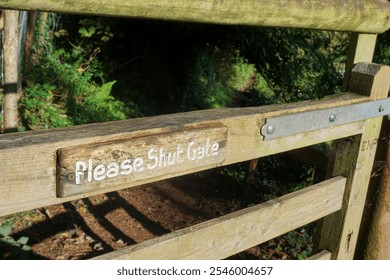 A countryside wooden gate with an engraved sign reading "Please Shut Gate." lush greenery, the scene evokes a sense of rural tranquility and respect for nature. - Powered by Shutterstock