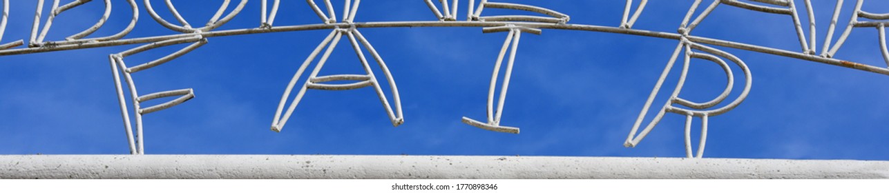 County Fair Sign Is Framed By Blue Sky.  Sign Is Made Out Of Iron And Painted White.