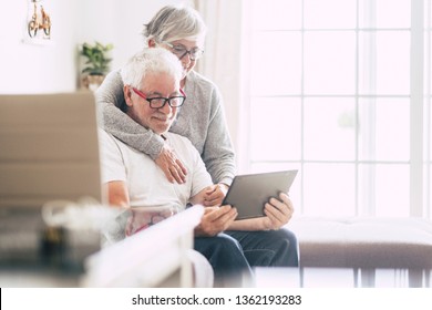 couple of adult seniors smiling and looking at the tablet - retired people using technology at home - woman hug the man with love - forever together nice old people enjoy technology
