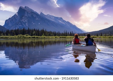 Couple adventurous friends are canoeing in a lake surrounded by the Canadian Mountains. Colorful Sunrise Sky Art Render. Taken in Vermilion Lakes, Banff, Alberta, Canada. - Powered by Shutterstock