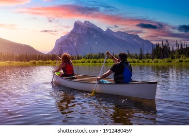 Couple adventurous friends are canoeing in a lake surrounded by the Canadian Mountains. Colorful Sunrise Sky Art Render. Taken in Vermilion Lakes, Banff, Alberta, Canada. - Powered by Shutterstock