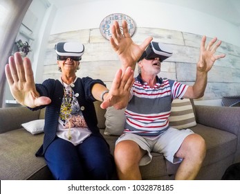 Couple of aged man and woman senior elderly play at home on the sofa with goggles headset trying virtual reality video games and vides. Activityies at home for 60 years old concept