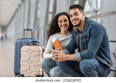 Couple In Airport. Happy Young Man And Woman Waiting For Flight At Terminal, Millennial Middle Eastern Spouses Relaxing Near Boarding Gate With Suitcases And Passports, Closeup Shot With Free Space