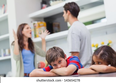 Couple arguing behind their children in the kitchen - Powered by Shutterstock