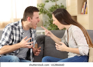 Couple arguing and screaming each other sitting on a sofa in the living room at home