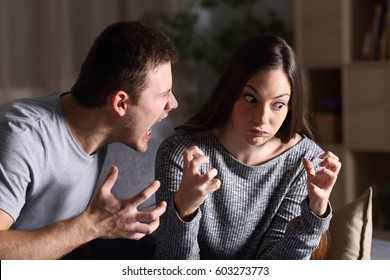 Couple arguing and shouting sitting on a couch in the living room at home with a dark background