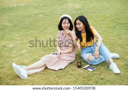 Couple of asian bestfriends sitting on glass field feeding cookie.