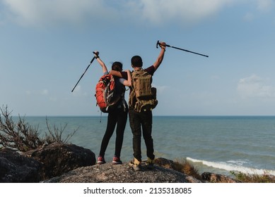 A Couple Of Asian Hikers Look At The Sea And Rejoice At Their Destination.