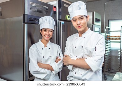 Couple asian young female bakers looking at camera..Chefs  baker in a chef dress and hat, cooking together in kitchen.Team of professional cooks in uniform preparing meals for a restaurant.