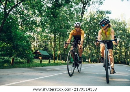 Couple of athletes dressed in active wear biking fast on paved road. Countryside area, sunny day outdoors. Professional road bicycle racers in action. Concept of endurance and strength. Copy space.