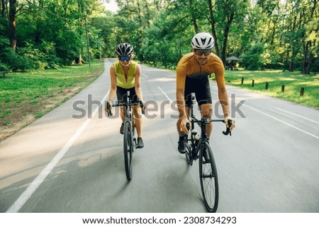 Couple of athletes dressed in activewear biking fast on paved road. Man and woman riding bikes outside of the city. Professional road bicycle racers in action. Concept of endurance and strength.
