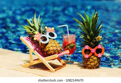 Couple of attractive pineapples in cheerful sunglasses lying on sunchair near the turquoise swimming pool. Relaxing, drinking fresh juice. Tropical summer vacation concept. Happy sunny day. Sunbathing - Powered by Shutterstock