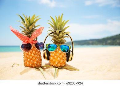 Couple of attractive pineapples in love on the sand against turquoise sea. Wearing stylish mirrored sunglasses. Tropical summer vacation concept. Sunny day on the beach of tropical island. Honeymoon 