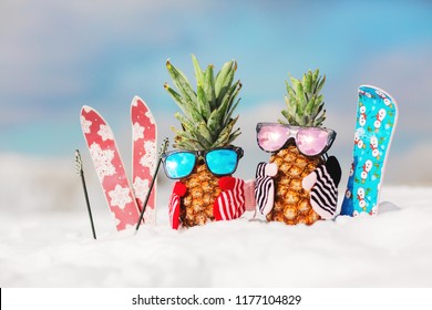 Couple of attractive pineapples in stylish mirrored sunglasses on the snow in the mountain. Winter ski holidays concept. Wearing stylish mittens. Mountain skiing, snowboard outfit. Family holiday
