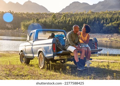 Couple With Backpacks In Pick Up Truck On Road Trip By Lake Drinking Beer - Powered by Shutterstock