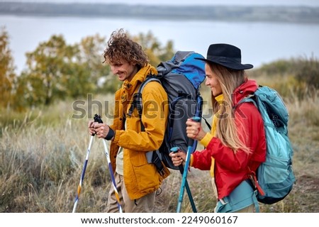 couple with bag pack on back holding hiking pole during hiking jurney, active athletic man and woman in colorful sportive outfit, vacation in nature outdoors. travel, sport, adventure concept