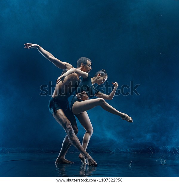 The couple of ballet dancers dancing under water\
drops and spray. Young caucasian and afro american models. Man and\
woman dancing together. Ballet and contemporary choreography\
concept. Art photo