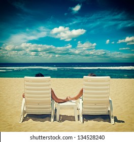 Couple in beach chairs holding hands near ocean. Cross processed vintage style