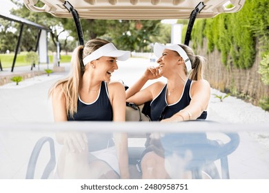 A couple of beautiful blonde girls have fun one day at a golf club.Young women are riding in a golf cart while talking happily.Concept of pretty women playing golf. - Powered by Shutterstock