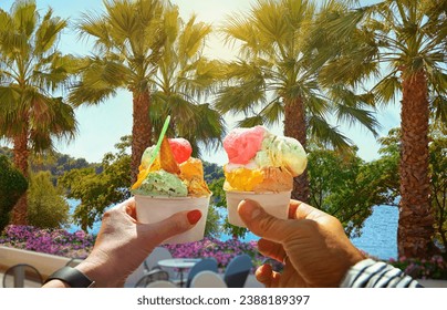 Couple with beautiful bright  sweet  ice-cream with different flavors  in the hands. Background of   view of the see with coconut palm trees in Porec ,Croatia.Traveling concept background - Powered by Shutterstock