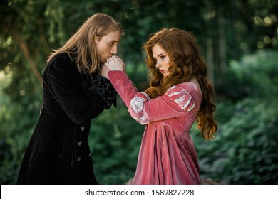 A couple of a beautiful young people posing in vintage medieval dresses on a nature background. Love story.