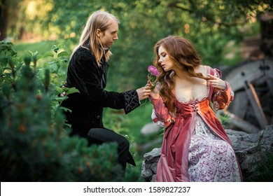 A couple of a beautiful young people posing in vintage medieval dresses on a nature background. Love story.