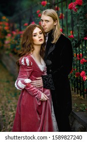 A couple of a beautiful young people posing in vintage medieval dresses on a nature background with roses. Love story.