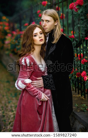 A couple of a beautiful young people posing in vintage medieval dresses on a nature background with roses. Love story.