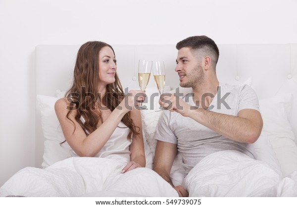 couple in bed toasting with champagne sparkling\
wine. celebrating honeymoon in romantic hotel room. millennials\
dating concept