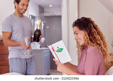 Couple In Bedroom As Man Holds Champagne As Woman Reads Card Celebrating Birthday Or Anniversary