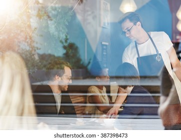 Couple Being Served By A Waiter In Busy Cafe