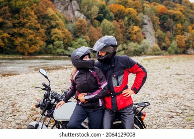 Couple of bikers travel by motorbike in fall. Motorcyclists enjoy autumn landscape in mountains having rest by forest and river. Man and woman standing by motorcycle
