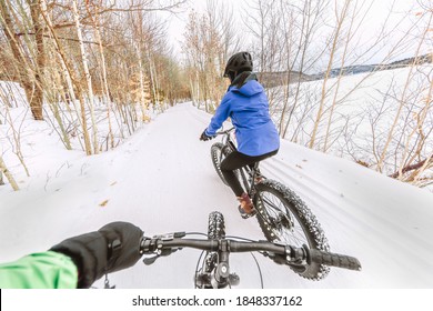 Couple biking on fat bikes on winter snow trail outdoor. Mountain nature landscape, woman rider cycling from behind with point of view of man holding handlebar of his bike.