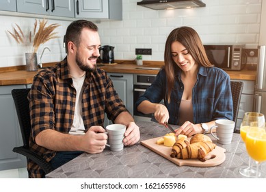 Couple At Breakfast. A Guy With A Cup Of Coffee, A Girl Cuts Cheese And Bread