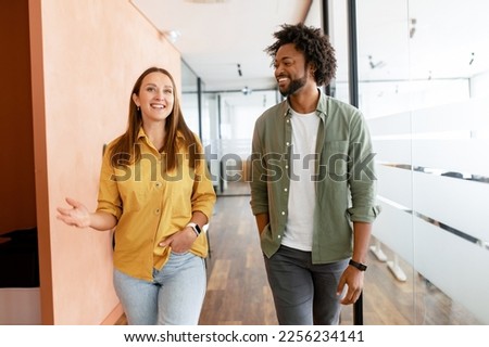 Couple of business people discussing tasks walking in the office hall. Two diverse colleagues have small talk during break. Friendly atmosphere in team