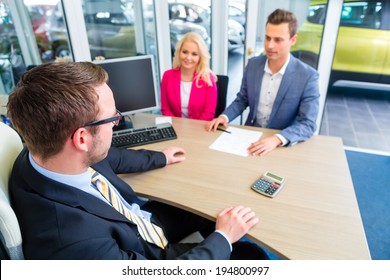 Couple Buying Car At Dealership And Negotiating Price With Salesman