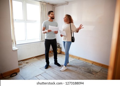 Couple Buying House For First Time Looking At House Survey In Room To Be Renovated