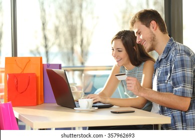 Couple Buying Online With Credit Card And Laptop With Shopping Bags In A Coffee Shop