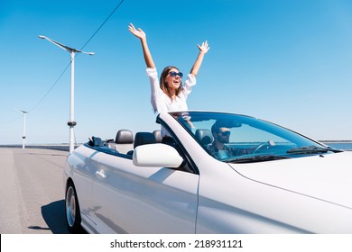 Couple in cabriolet. Happy young couple enjoying road trip in their convertible while woman raising arms and smiling  - Powered by Shutterstock