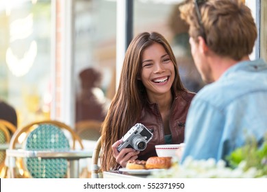 Couple at cafe lifestyle. Young tourists eating breakfast at restaurant table outside sidewalk terrace at parisian bistro in european city. Asian woman traveler with vintage camera. Europe tourism.